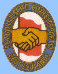 Emblem: Handschlag zwischen KPD und SPD vor der roten Fahne der Arbeiterklasse auf weißem Grund, Parteiname als Umschrift auf blauem Grund